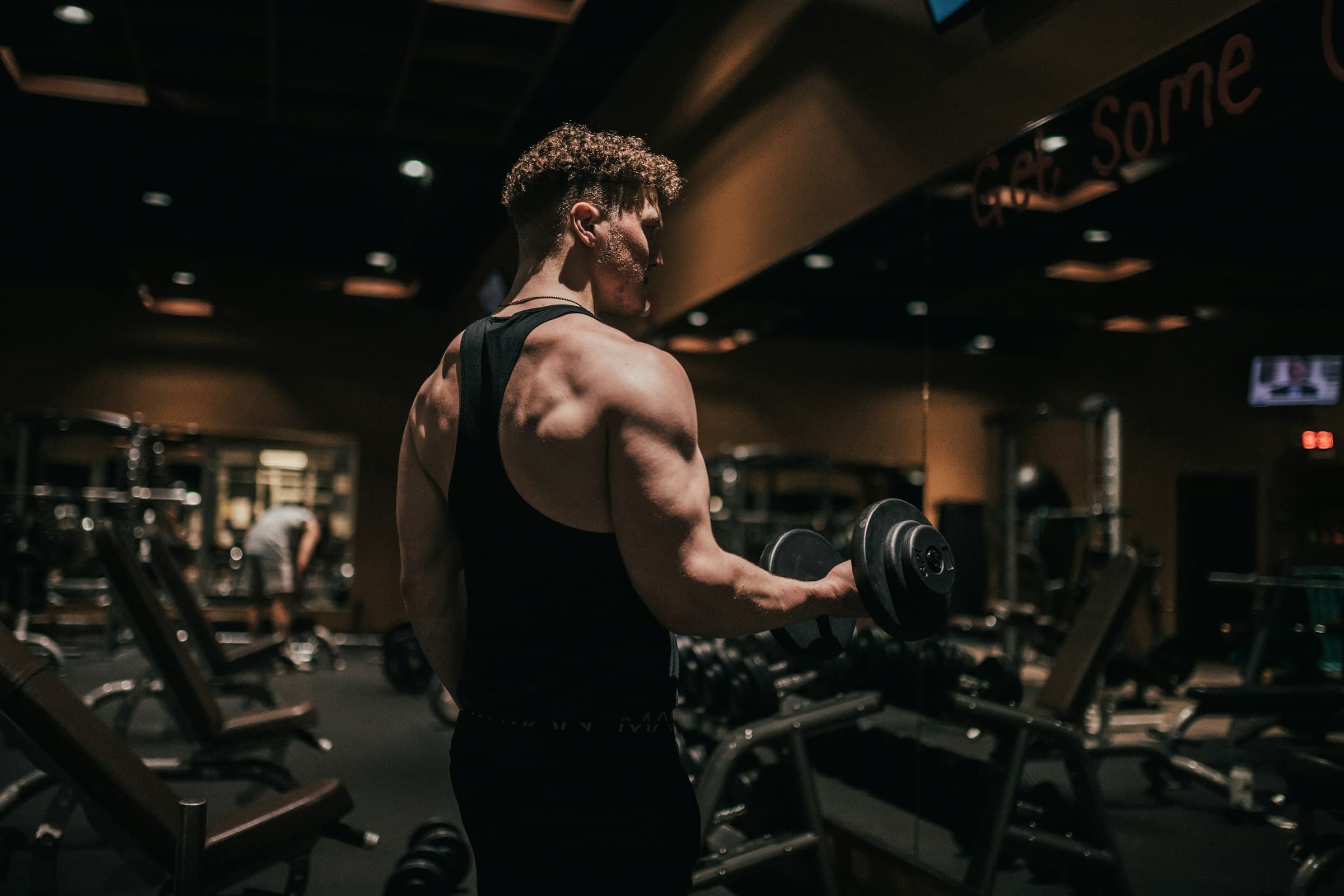 A man holding a dumbbell between sets in a dim gym